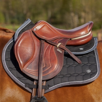 Sela de cavalo castanha em couro com manta preta e detalhes cinza montada num cavalo