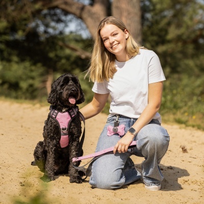 Cão preto com peitoral cor-de-rosa e mulher sorridente ao ar livre