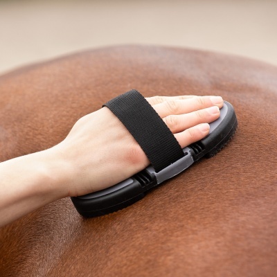 Escova de mão preta com alça elástica sendo usada em pelo castanho de cavalo