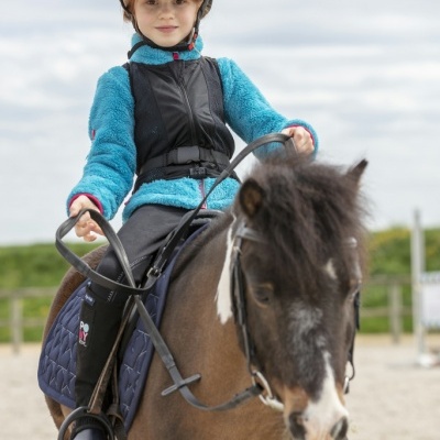 Criança montada num cavalo castanho com mancha branca, usando equipamento de equitação