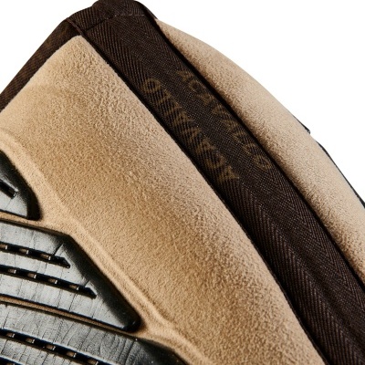 Detalhe de um calçado esportivo bege com sola preta e faixa marrom com texto