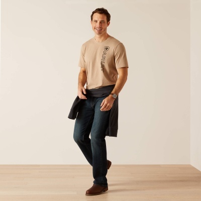 Homem com t-shirt bege, jeans azul escuro e casaco preto amarrado à cintura