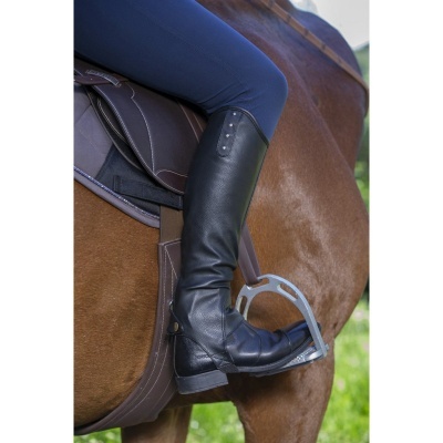 Bota preta de montaria em pele com botões metálicos usada a montar em cavalo castanho