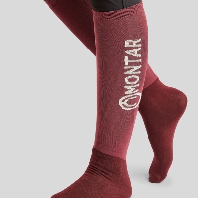 Meias altas bordeaux com logotipo MONTAÑER branco usadas por pessoa com calças pretas.