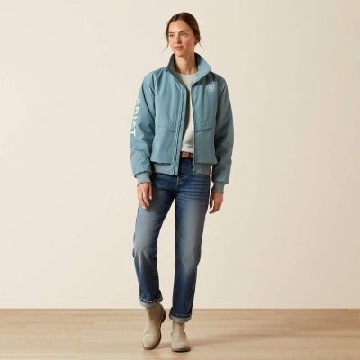 Mulher com jaqueta azul e jeans em fundo claro e chão de madeira