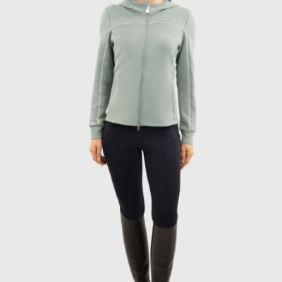 Mulher com casaco cinza claro, calças pretas, botas pretas e boné cinza com letra H