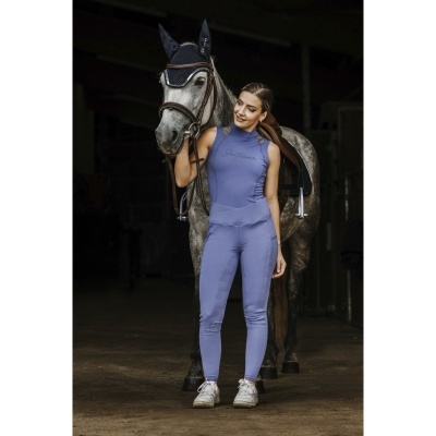 Conjunto desportivo de equitação azul lilás com top e calças junto a cavalo cinzento em cavalariça