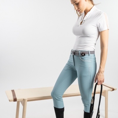 Mulher com roupa de equitação segurando guia preta ao lado de banco de madeira clara