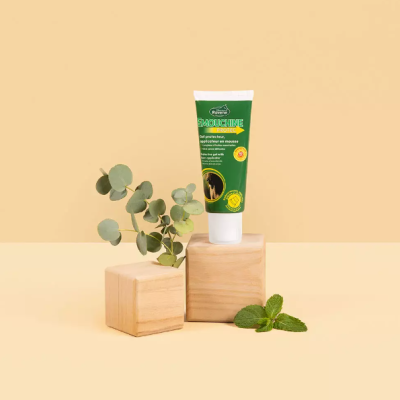 Tubo verde de creme sobre suportes de madeira com ramos verdes e planta de hortelã ao lado