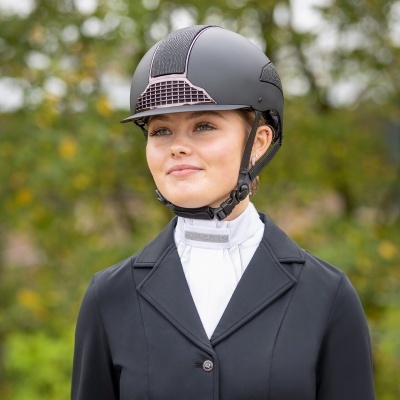 Mulher com capacete de equitação preto, casaco preto e camisa branca ao ar livre