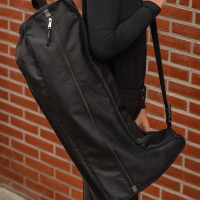 Bolsa comprida preta com fecho e alça, roupa preta, parede de tijolos vermelhos