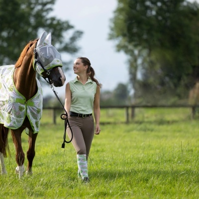 Cavalo com manta branca e padrão verde ao lado de mulher no campo verde