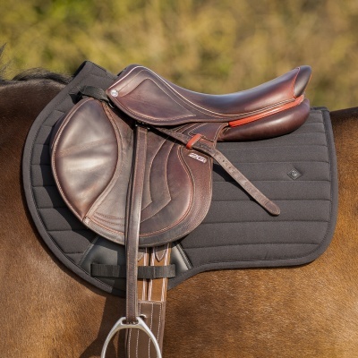 Sela de equitação em pele castanha escura com detalhes vermelhos sobre um cavalo castanho e uma manta preta acolchoada