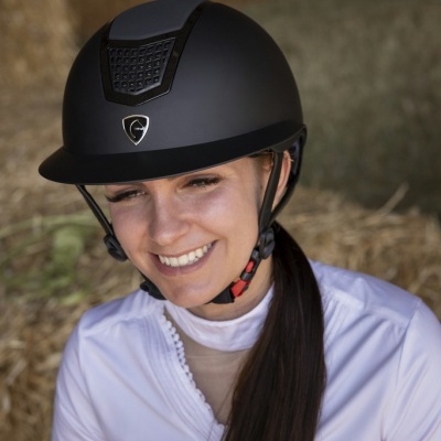 Mulher sorridente usando capacete de equitação preto em ambiente de feno