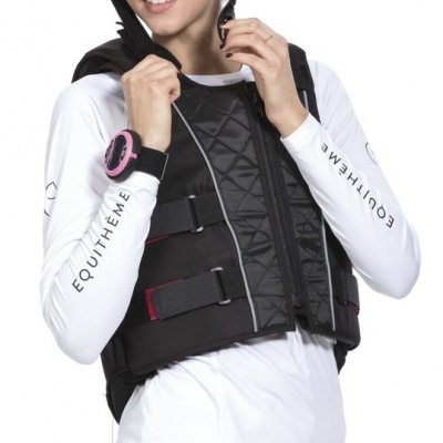 Mulher com capacete e colete de proteção preto, camisa e calças brancas com texto EQUITHÈME nas mangas