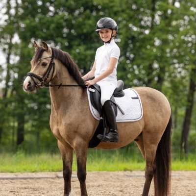 Menina montada num cavalo castanho claro com equipamento de equitação em campo de terra batida