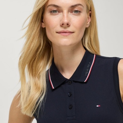Mulher a usar top polo azul escuro sem mangas com detalhes nas cores vermelho, branco e azul na gola e logótipo no peito