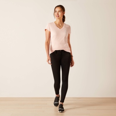 Mulher com t-shirt rosa clara e calças pretas numa parede branca