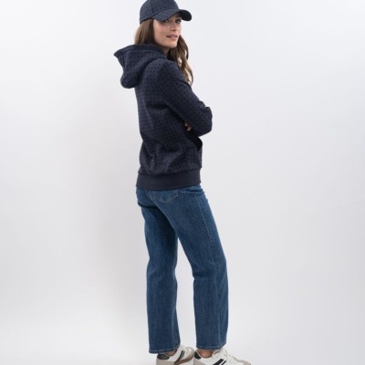 Mulher com boné e sweat azul escuro com padrão, jeans azuis e sapatilhas brancas.