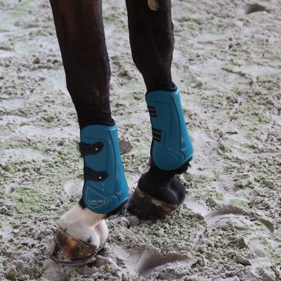 Pernas de cavalo com escoras de proteção azuis em chão de areia com pegadas