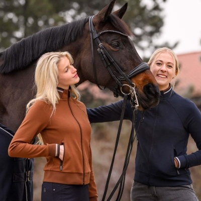 Duas mulheres em casacos desportivos e cavalo com arreio preto ao ar livre