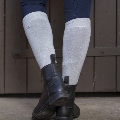 Pernas de pessoa com leggings azuis, meias cinza e botas pretas junto a porta de madeira escura.