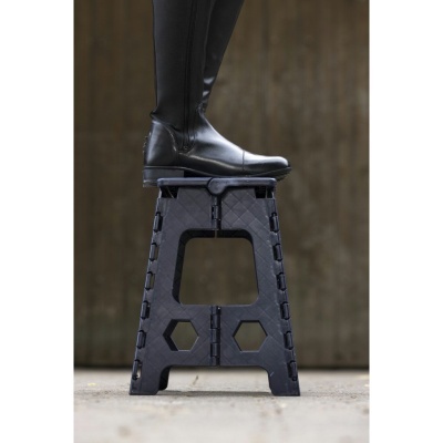 Banqueta preta de plástico com padrões hexagonais e recortes, com pessoa a calçar botas pretas.