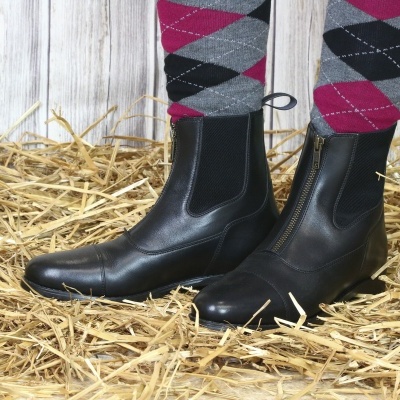 Botas pretas de couro com fecho frontal e meias xadrez coloridas sobre palha