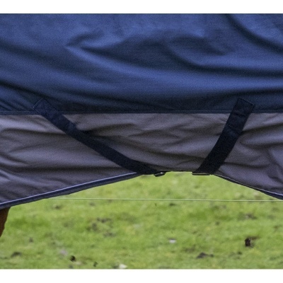 Cobertura azul e cinza com fecho e tiras negras sobre animal, fundo de relva