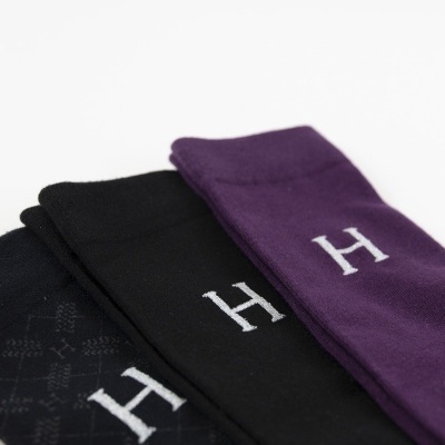 Três pares de meias nas cores preto e roxo com a letra H branca.