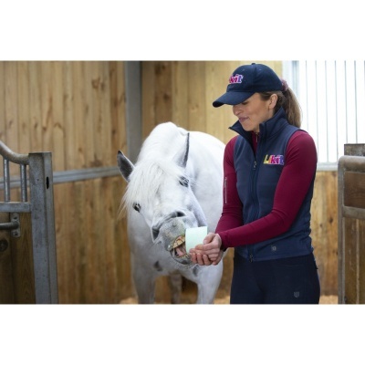 Mulher a alimentar cavalo branco com casaco e boné azul escuro com logo Likit em estábulo de madeira