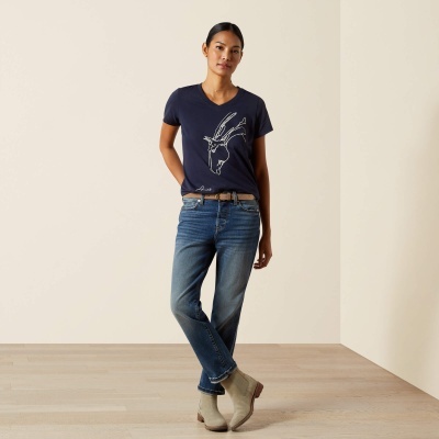 Modelo feminino com camiseta azul escura com estampa de cabra, jeans azuis, cinto castanho e botas bege