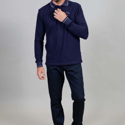 Homem a usar camisa azul de manga comprida com gola e punhos com risca branca, calças azul escuras e ténis brancos