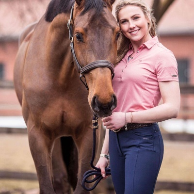 Mulher com camisa rosa e calças azuis com cavalo castanho ao ar livre.