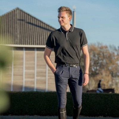 Homem com polo preta, calças azuis e botas pretas ao ar livre