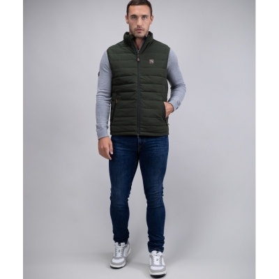 Homem com colete acolchoado verde, camisola cinzenta, calças jeans azuis e ténis brancos