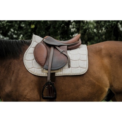 Sela de equitação em couro castanho escuro com manta branca acolchoada sobre cavalo castanho.