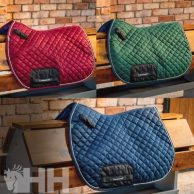 Três mantas de sela em vermelha, verde e azul acolchoadas com etiquetas Horseware sobre madeira