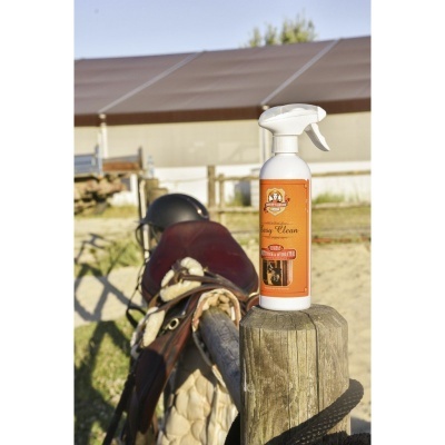 Frasco de spray branco com rótulo laranja sobre poste de madeira ao lado de sela de cavalo castanha