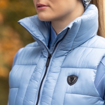 Mulher vestindo colete azul claro acolchoado com emblema triangular preto no peito
