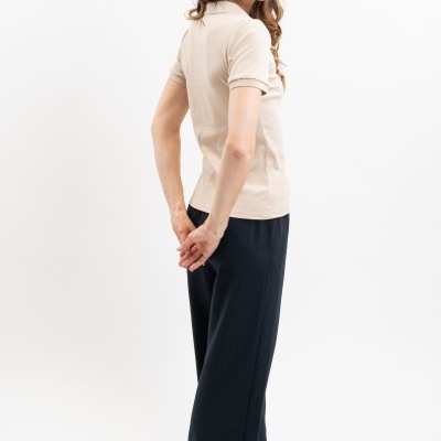 Mulher de perfil com polo bege, calças pretas largas e óculos de sol