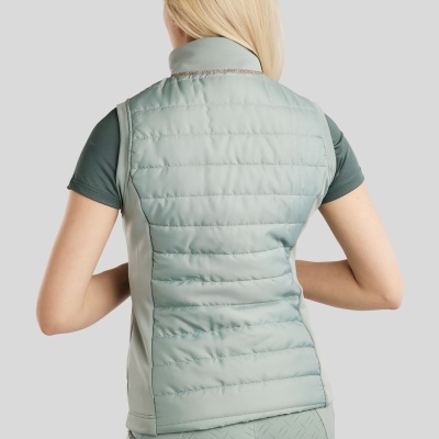 Mulher vista de costas usando colete matelassê verde com calças desportivas e camiseta verde.