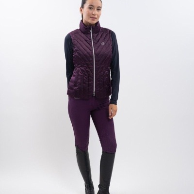 Mulher com colete roxo matelassê, leggings roxas e botas pretas em fundo branco