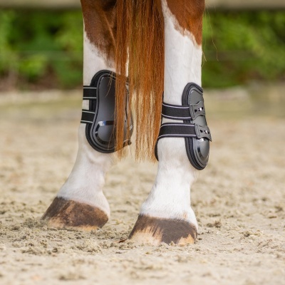 Pernas de cavalo com proteções negras de equitação em solo arenoso