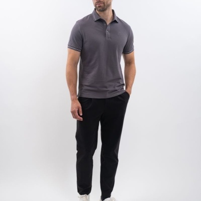 Homem com polo cinzenta escura e calças pretas em fundo branco