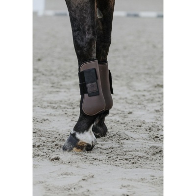 Cavalo com botas protetoras castanhas e tiras pretas em piso de areia