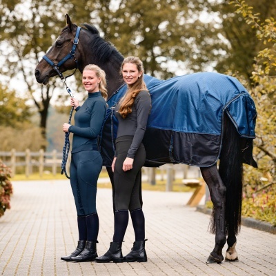 Cavalo com manta azul e duas mulheres em roupas de equitação e botas pretas ao ar livre