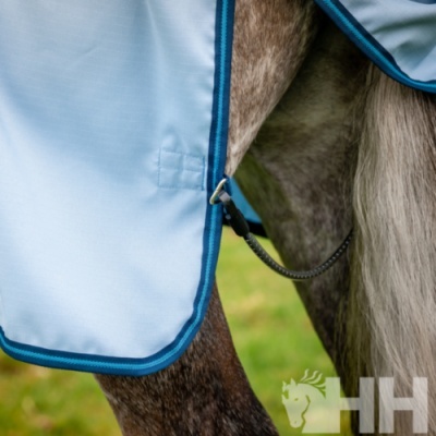Manta azul clara para cavalo com bordos azuis escuros e corda preta, em corpo de cavalo castanho e branco em relvado.