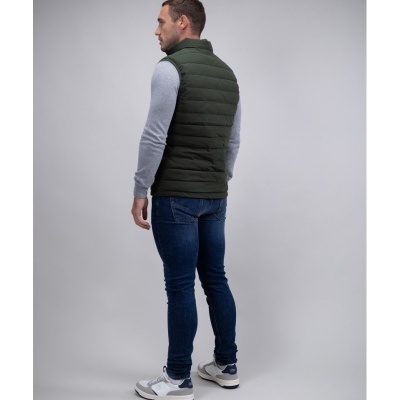 Homem de costas com colete verde, camisola cinza, jeans e sapatilhas brancas e cinza