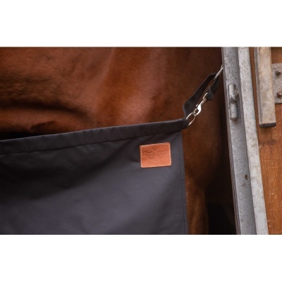 Protetor de tecido preto com etiqueta castanha em couro e fecho de metal junto a cavalo castanho